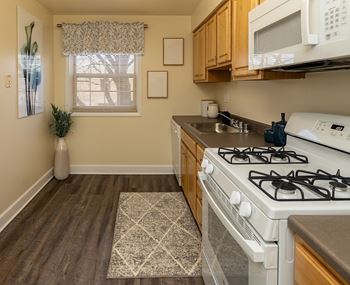 Kitchen with white appliances and wooden cabinets at Painters Mill Apartments, Randallstown
